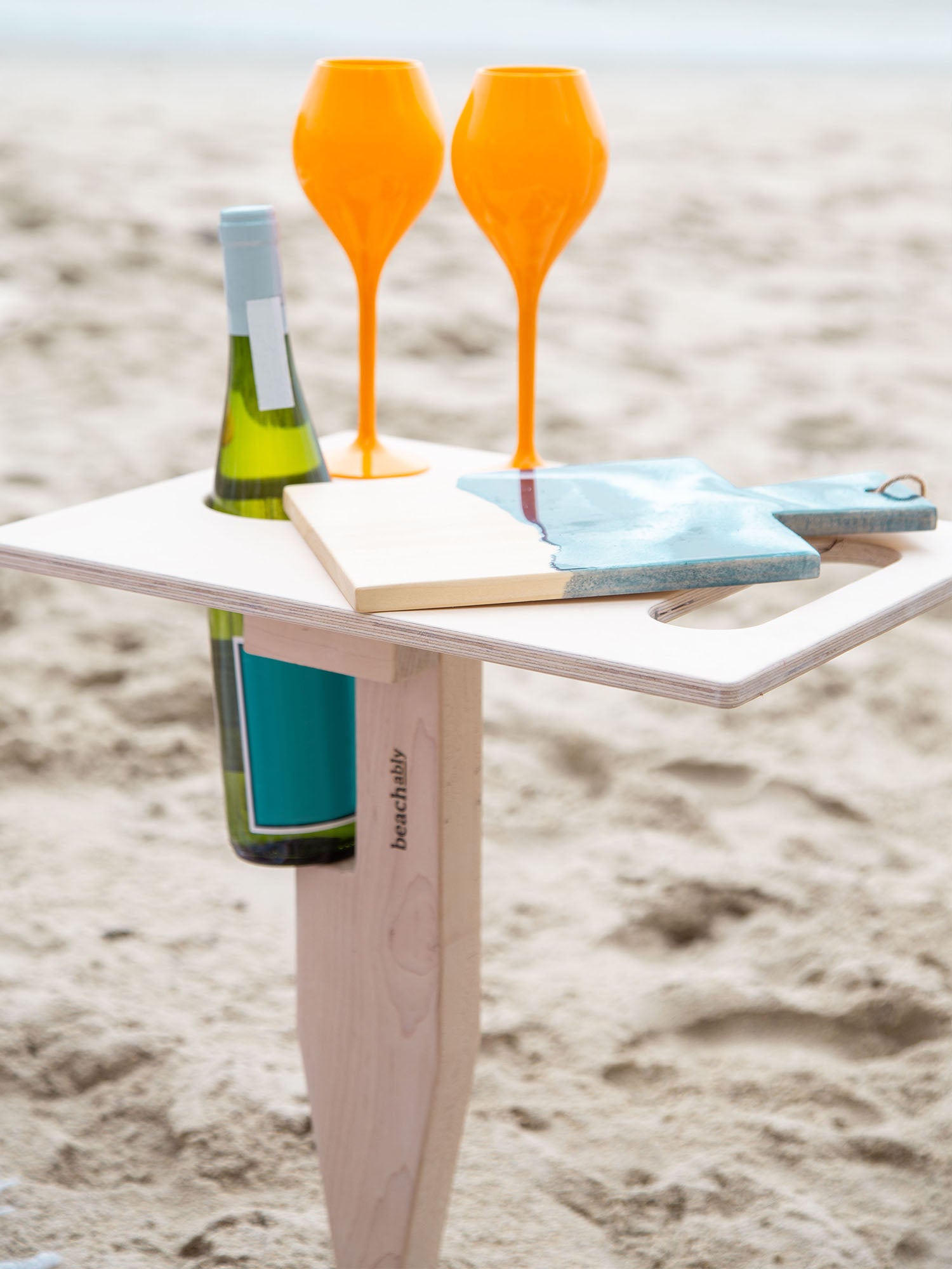 Esplanade portable beach table in beach blonde color unfolded standing up in sand at beach with refreshment drinks